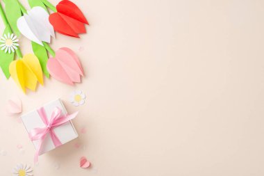 Origami laleleri, papatya çiçekleri, kurdeleli DIY hediye kutusu, kağıt kalpler ve pastel bej bir alanda ince konfetilerin yanında yaratıcı Anneler Günü konsepti.
