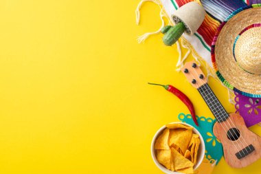 Cinco de Mayo parti sahnesi. Temel elementlerin üst görüntüsü: canlı sombrero, vihuela, bir kaktüs, bir serape, bir ipte bayraklar, kırmızı biber, nachos, hepsi sarı arka planda, mesaj için yer tutucu