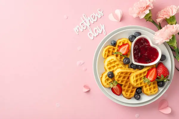 Special Mother\'s Day breakfast arrangement: top view shot of table with heart waffles, strawberries, blueberries, marmalade, flowers, \