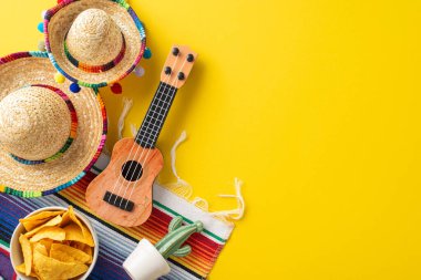Cinco de Mayo gösterisi. Temel sembolleri yakalamak için üstten bir görüntü: kompakt sombreros, halk vihuela, saksıdaki kaktüs, canlı bir serape, ve hardal sarısı bir tabanda bir porsiyon nacho.