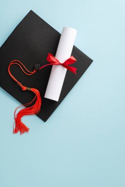 Harç tahtasının dikey manzarasına sahip akademik başarılar ve mesajınız veya reklam ihtiyaçlarınız için tasarlanmış, sakin pastel mavi yüzeyde kurdele yayıyla bağlanmış diploma.