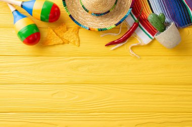 Şenlikli Cinco de Mayo üst görünümü. Sombrero, maracas ve kaktüslerle donatılmış. Canlı serape, nacho ve kırmızı biber sarı ahşap masayı süslüyor. Metin için boşluk olan üst görünüm
