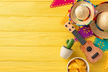 Cinco de Mayo üst manzara: sombreros, vihuela, ve sergilenen bir kaktüs. Renkli bayrak çelengi ve sarı ahşap masayı süsleyen baharatlı nacho. Metin için boşluk