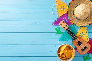 Cinco de Mayo 'yu bu renkli üst manzara düzenlemesiyle kutlayın: sombrero, vihuela, bayrak çelengi, ahşap mavi arka planda nachos. Promosyon malzemeleri için ideal