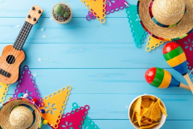 Cinco de Mayo için Meksika temalı bir anlaşma. Kültürel eşyalar: sombreros, vihuela, maracas, kaktüs, bayrak çelenkleri ve mavi ahşap yüzeyde nachos. Olay tanıtımları için ideal