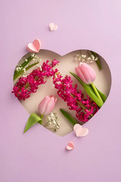Celebrate Mom\'s Day: Vertical top view of tulips, hyacinth, gypsophila, paper hearts artfully arranged under heart-shaped cutout frame on pastel violet. Ideal backdrop for messages or advertisements