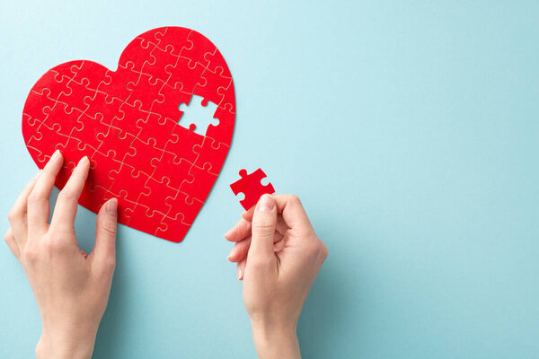 First person top view photo of female hands creating a heart-shaped puzzle with jigsaw piece on a pastel blue background for World Blood Donor Day