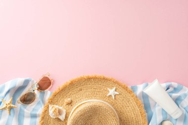 Hasır şapkanın üst görüntüsü, şık güneş gözlükleri, denizyıldızı ve güneş kremi, yumuşak pembe arka planda çizgili bir kumaş üzerinde düzgünce serilmiş. Plaj tatili ve yaz tatilinin mükemmel tasviri