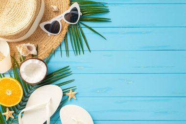 Güneş gözlüğü, şapka, parmak arası terlik, hindistan cevizi ve turkuaz rengi ahşap bir yüzey üzerinde portakal gibi canlı bir yaz plaj eşyası koleksiyonu ideal tatil atmosferini resmediyor.