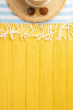 Tropikal fantezi gözler önüne serildi: dikey üst görünüm hasır şapka, güneş gözlüğü, plaj battaniyesi, güneşli sarı bir yüzey üzerinde