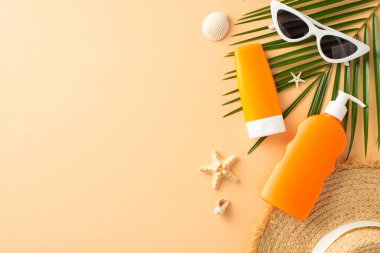 Güneş kremi, güneş gözlüğü ve palmiye yapraklarından oluşan bej arkaplan üzerine plaj aksesuarları.