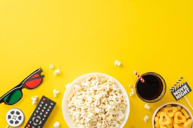 Evde rahatlatıcı sinema deneyimi: Kıtır kıtır patlamış mısır, cips, soda, 3 boyutlu bardaklar. Çevrimiçi yayın için uzaktan kumanda. Sarı arkaplan üzerine filmden esinlenilmiş dekorasyonlar, metin veya reklamlar için boşluk