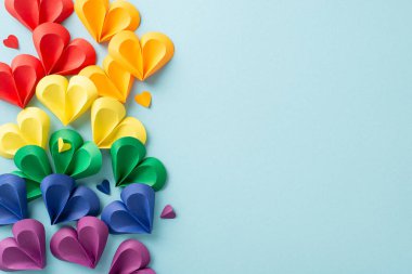 Renkli kağıt kalplerin gökkuşağı renklerinde dizilişi açık mavi bir arkaplana yayılmış gurur ayında aşkı ve çeşitliliği sembolize ediyor