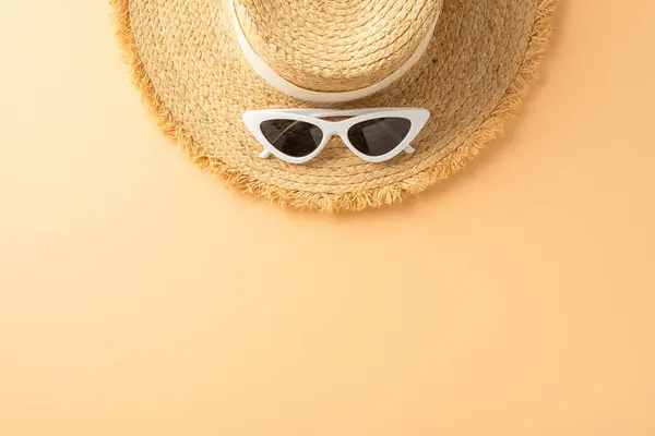 Top view of a straw hat with white band and white sunglasses laid on a yellow surface, symbolizing summer and sun protection