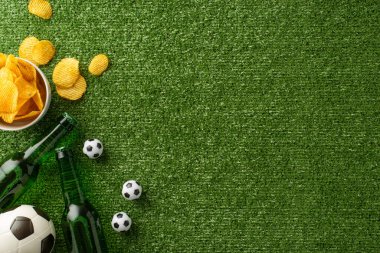 Futbol temalı abur cubur aranjmanının üst görüntüsü. Kasede cipsler, mini futbol topları ve çimlerin üzerinde dokulu bira şişeleri.