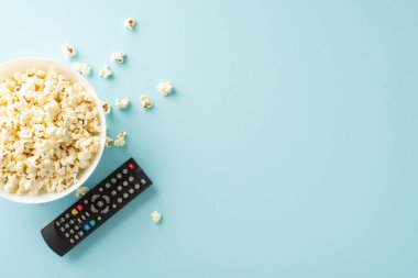 TV uygulaması kullanarak ev sinemasının tadını çıkarın. Patlamış mısırın en iyi görüntüsü ve pastel mavi arka planda çevrimiçi görüntüleme için uzaktan kumanda