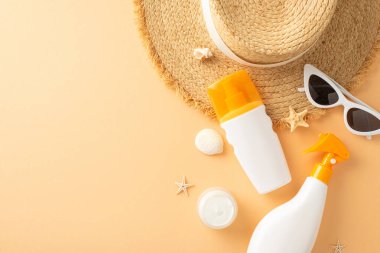 Güneş kremi, hasır şapka, güneş gözlüğü ve deniz kabuklarının yer aldığı bej bir yüzeyde düzgünce dizilmiş yaz plajı aksesuarlarının üst görüntüsü.