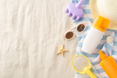 Çocuk kumsalı oyuncakları, güneş kremi, güneş gözlüğü ve havluya yerleştirilmiş bir hasır şapka.