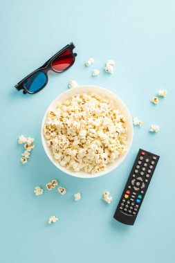 Evdeki TV uygulaması vasıtasıyla prömiyerlere dalın. Patlamış mısırın dikey üst görünümü, 3D gözlükler, çevrimiçi görüntüleme için uzaktan kumanda, pastel mavi arkaplan üzerine kurulmuş