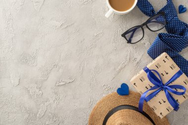 Bir hediye kutusu, mavi kravat, kahve fincanı, bardaklar ve desenli beton bir yüzeye yerleştirilmiş şapka içeren düşünceli bir Babalar Günü düzeneği.