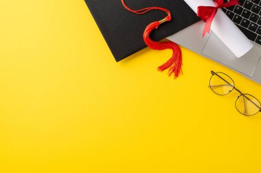 Uzaktan öğrenme başarısı. Dizüstü bilgisayarın üst görünümü, mezuniyet şapkası, diploma, çalışma araçları, sarı arkaplandaki gözlükler metin veya reklam alanı