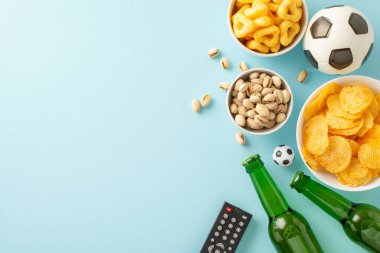 Euro 2024 'ü futbol fanatikleri için bir ziyafetle kutlayın: uzaktan kumanda, futbol topu, cips, fıstık, cips, buz gibi bira. Açık mavi yüzey üzerindeki en üst görünüm, metin veya promosyonlar için yer sağlar
