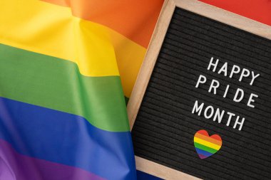 LGBTQ + gururu simgeleyen canlı bir gökkuşağı bayrağının yanındaki siyah harf panosundaki Mutlu Onur Ayı mesajı