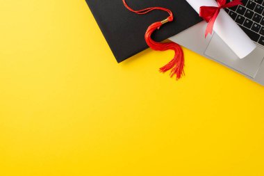 Kırmızı püsküllü mezuniyet şapkasını gösteren canlı bir görüntü dizüstü bilgisayarın üzerinde sarı bir arkaplanda duruyor. Modern, sanal mezuniyetlerin özünü mükemmel bir şekilde yansıtıyor.