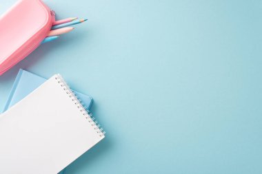 Okula geri dönen bir minimalist pembe kalem kutusu, renkli kalemler ve mavi arka planda boş bir defter.