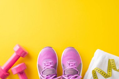 Sağlık çantası. Sarı arkaplanda spor ayakkabılarının, dambılların, havlunun ve mezuranın en üstteki görüntüsü.