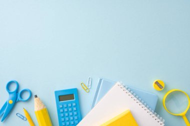 Kalemler, makas, defterler ve açık mavi bir arkaplanda düzenlenmiş hesap makinesi de dahil olmak üzere renkli okul malzemeleri.