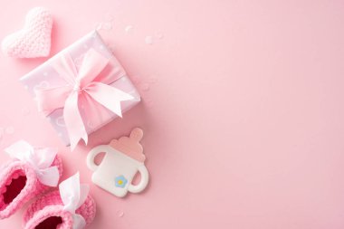 Paketli bir hediye paketi, bebek oyuncağı, pembe bebek ayakkabıları ve pembe arka planda örülmüş bir kalp.