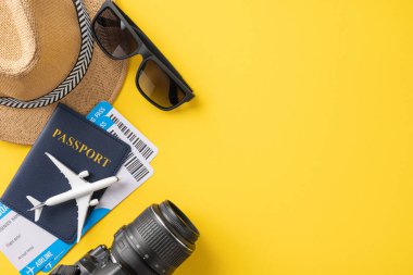 Pasaport, uçak biletleri, şapka, güneş gözlüğü ve parlak sarı arka plandaki kamera da dahil olmak üzere yaz seyahatinin temel gereksinimlerinin düz bir görüntüsü.