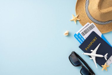 Seyahat gereksinimlerinin üst görüntüsü pasaport, biniş kartı, güneş gözlüğü, şapka ve açık mavi arka planda ayarlanmış denizyıldızı dahil.
