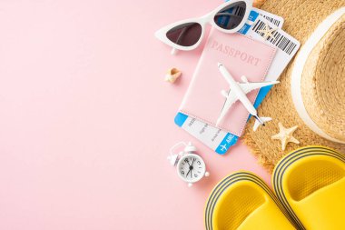 Pasaport, uçak biletleri, güneş gözlükleri, plaj şapkası ve pembe arka plandaki sandaletler de dahil olmak üzere yaz seyahatlerinin temel gereksinimleri.