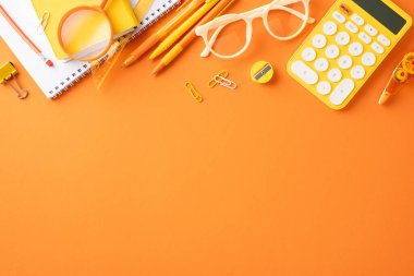 Not defterleri, kalemler ve turuncu bir masaya yayılmış hesap makinesi gibi çeşitli okul malzemelerinin üst görüntüsü.