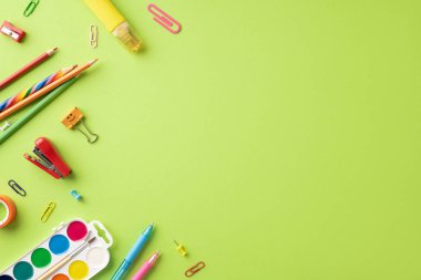 Açık yeşil arka planda kalemler, kalemler ve ataçlar dahil çeşitli okul malzemeleri. Okul temaları için ideal