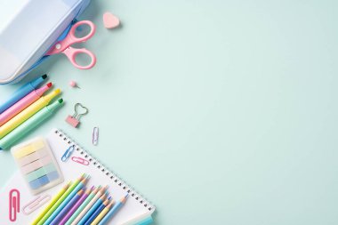 Kalemler, makas ve kağıt ataçları da dahil olmak üzere, hafif pastel arka planda renkli okul kırtasiyesi öğeleri