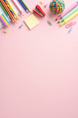 Kalemler, kalemler, yapışkan notlar ve pembe arka planda ataçlar da dahil olmak üzere okul malzemelerinin renkli dikey çeşitliliği