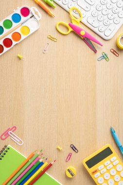 Klavye, hesap makinesi ve defterlerle ahşap masa arkasındaki çeşitli renkli okul malzemelerinin dikey üst görünümü