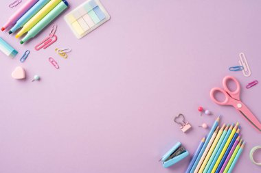 Renkli okul kırtasiyesinin üst görünümü. Mor renkli bir arka planda kalem, kalem ve makas da dahil.