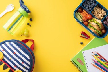 Temiz sebzeler, su şişesi ve parlak sarı arka planda okul malzemeleriyle sağlıklı bir okul atıştırmalığının en üst görüntüsü.