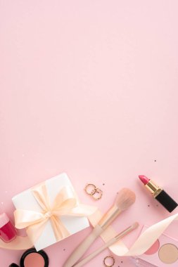Çeşitli dikey makyaj ürünleri ve pembe arka planda fiyonklu hediye kutusu. Güzellik ve kozmetik temalar için mükemmel.