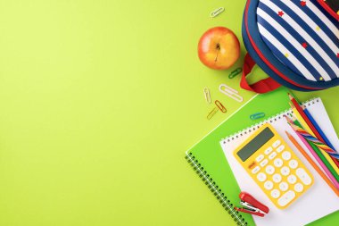 Yeşil arka planda, çizgili sırt çantası ve elmalı çeşitli okul malzemeleri. Okul konseptine dönelim.