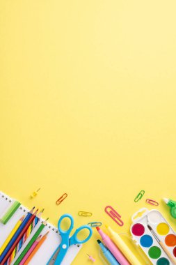 Kalemler, makaslar, ataçlar ve ataçlar da dahil olmak üzere parlak, dikey sarı bir zemin üzerine kurulmuş okul gereçlerine renkli geri dönüş