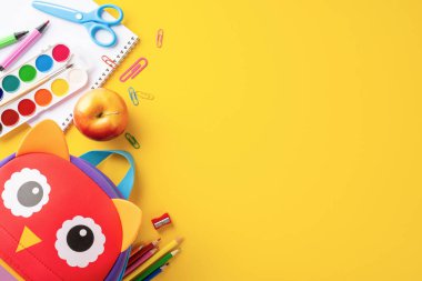 Bir baykuş çantası, makas, keçeli kalem ve sarı arka planda bir elma gibi çeşitli renkli kırtasiye malzemelerini içeren okul konseptine geri dönelim.