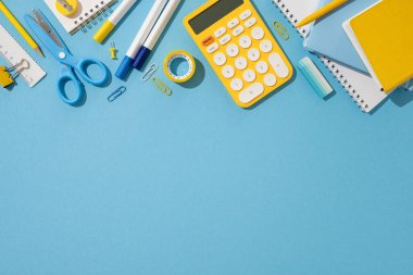 Hesap makinesi, makas ve mavi arkaplan üzerine not defterlerini içeren okul malzemelerinin düzlüğü
