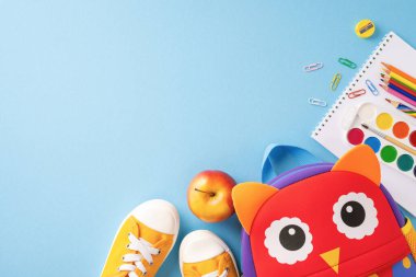 Okula dönüş için gerekli şeylerin en üst görüntüsü. Mavi arka planda ayakkabı, sırt çantası, elma ve okul malzemeleri de dahil.