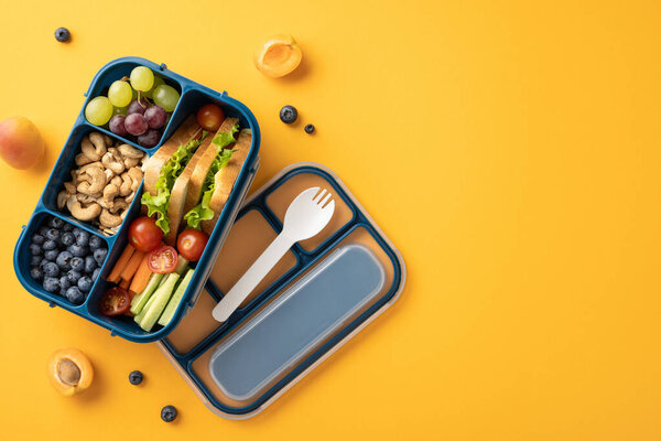 Здоровый школьный обед со свежими фруктами, овощами, орехами и бутербродом на ярко-желтом фоне
