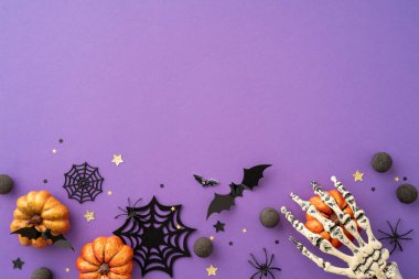 Cadılar Bayramı temalı arka planda balkabakları, yarasalar, örümcek ağları, iskelet eller ve mor bir yüzey üzerindeki tatil süslemeleri yer alıyor.